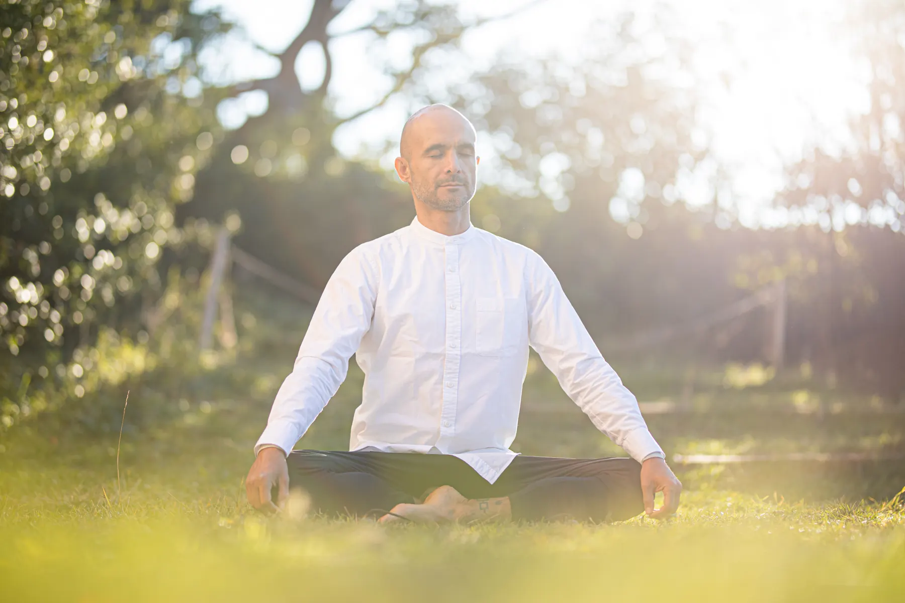Andrei Ram sentado en meditación sobre la hierba, a contraluz
